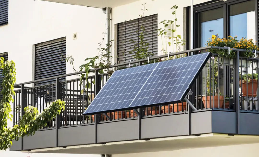 Solar panel mounted on an apartment balcony railing, surrounded by potted plants and flowers, providing renewable energy for the home.